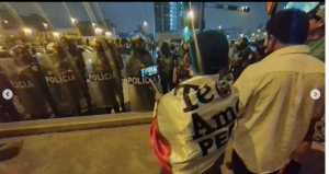 hombre peruano con una bandera peruana amarrada a la espalda mira a un grupo de policías 