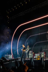 Imagen del concierto de Los Bunkers, en la que resalta Álvaro López en el escenario, bajo unas lineas de luz roja