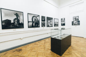 En la imagen se ve la Sala de Artes Visuales de la Usach. Se ven varias obras expuestas en la pared.