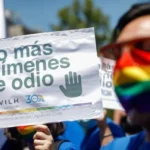Cartel blanco y cuadrado que dice con letras negras "no más crimenes de odio". Abajo dice, en letras más pequeñas, MOVILH y XXI conmemoración del orgullo en Chile. La foto se tomo en un desfile del orgullo.