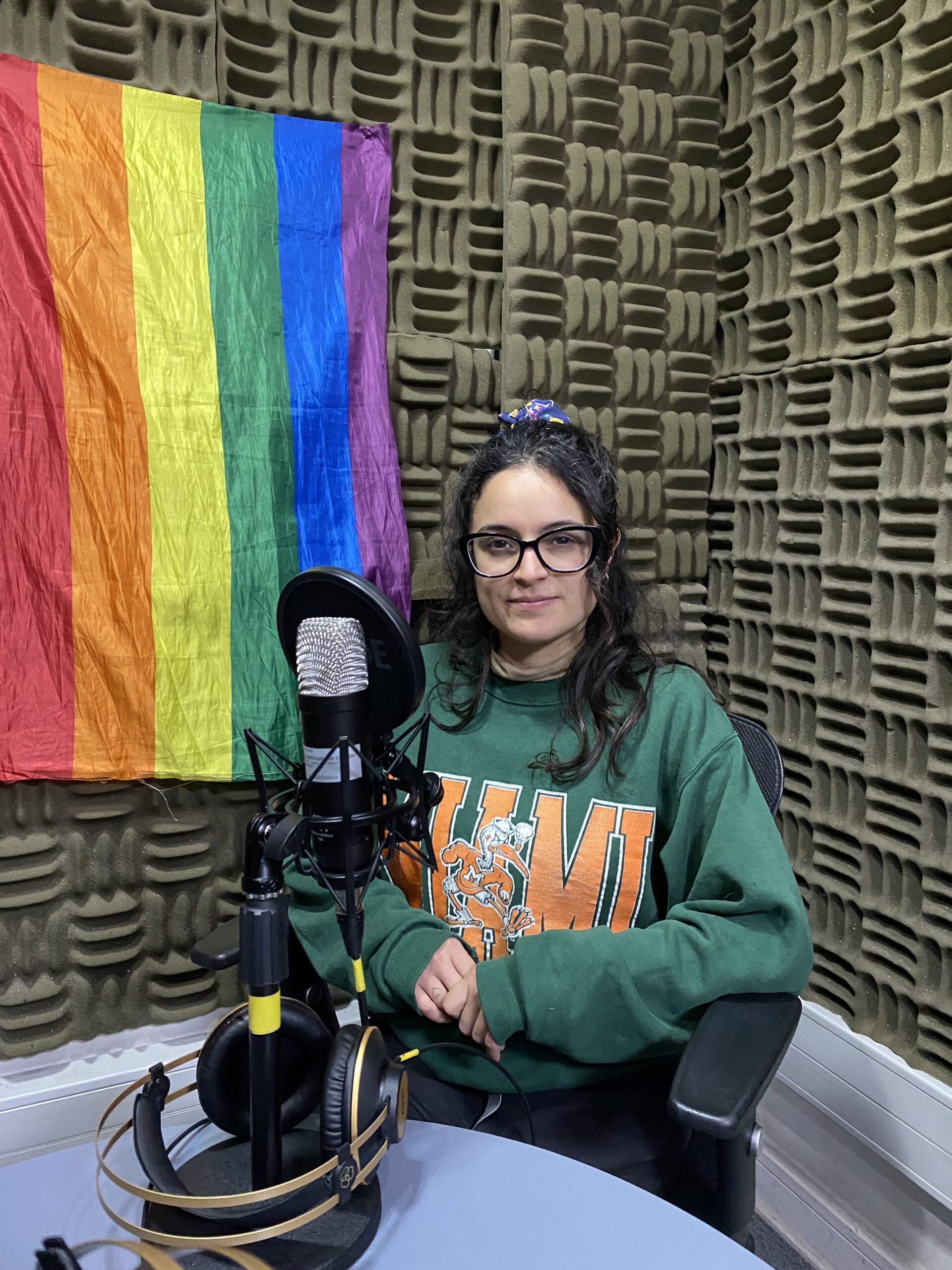 Mujer sentada en un estudio de radio con una abndera lgbt detras