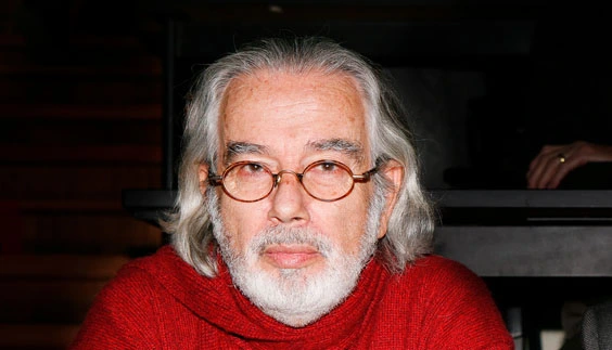 Al centro, Miguel Kottow. Viste un poleron rojo, lleva barba blanca y cabello también blanco largo. Usa lentes rojos.