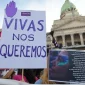 A la izquierda: cartel blanco con una mano morada y letras moradas que dicen "Vivas nos queremos". A la derecha arriba un edificio blanco antiguo y abajo un cartel con una mujer y letras blancas.