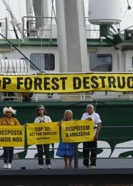 Cuatro personas con carteles frente a un barco en una manifestación pacifica