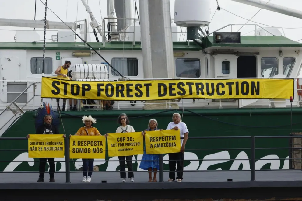 Cuatro personas con carteles frente a un barco en una manifestación pacifica
